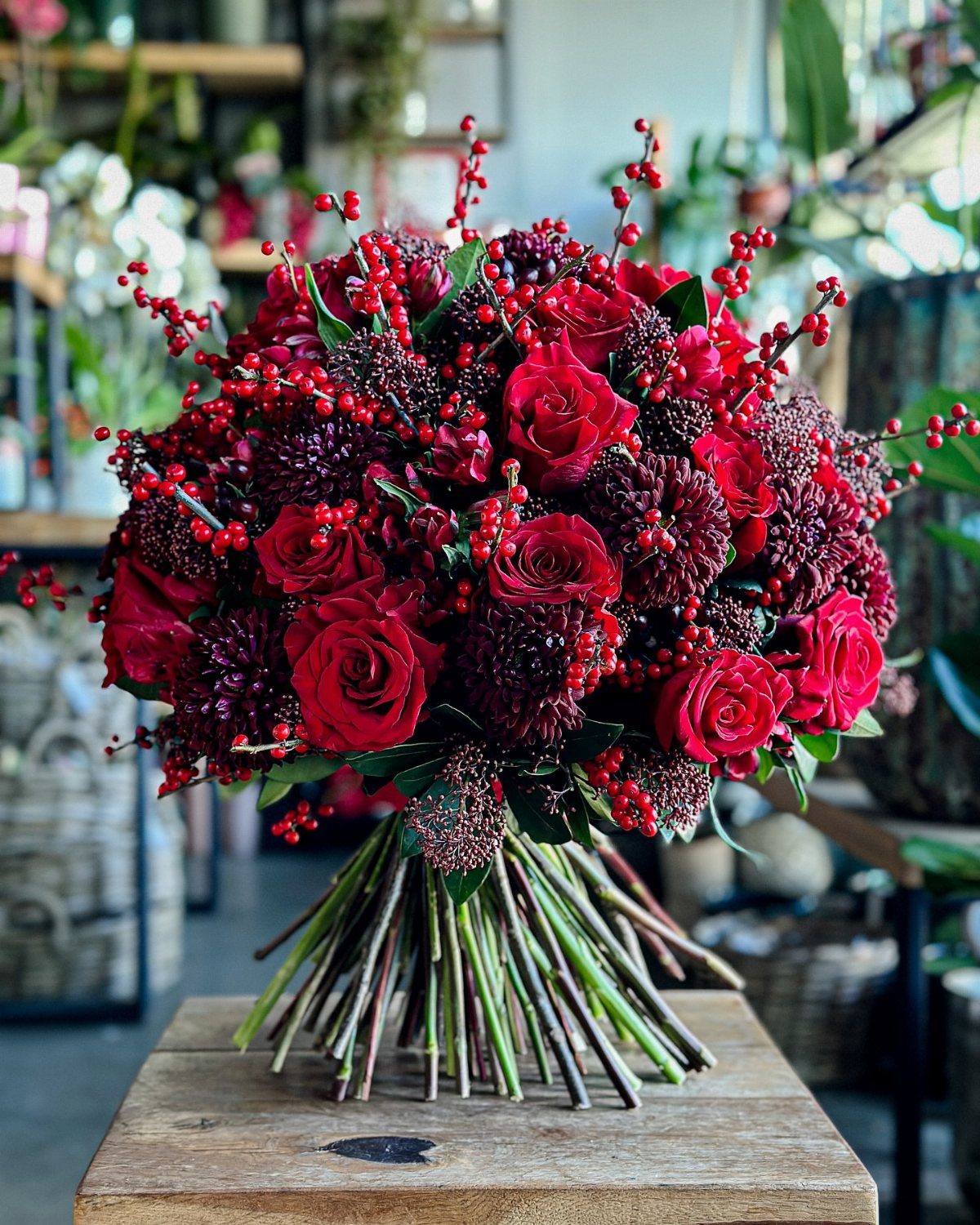 Red roses and burgundy flowers with red berries in a festive holiday bouquet.