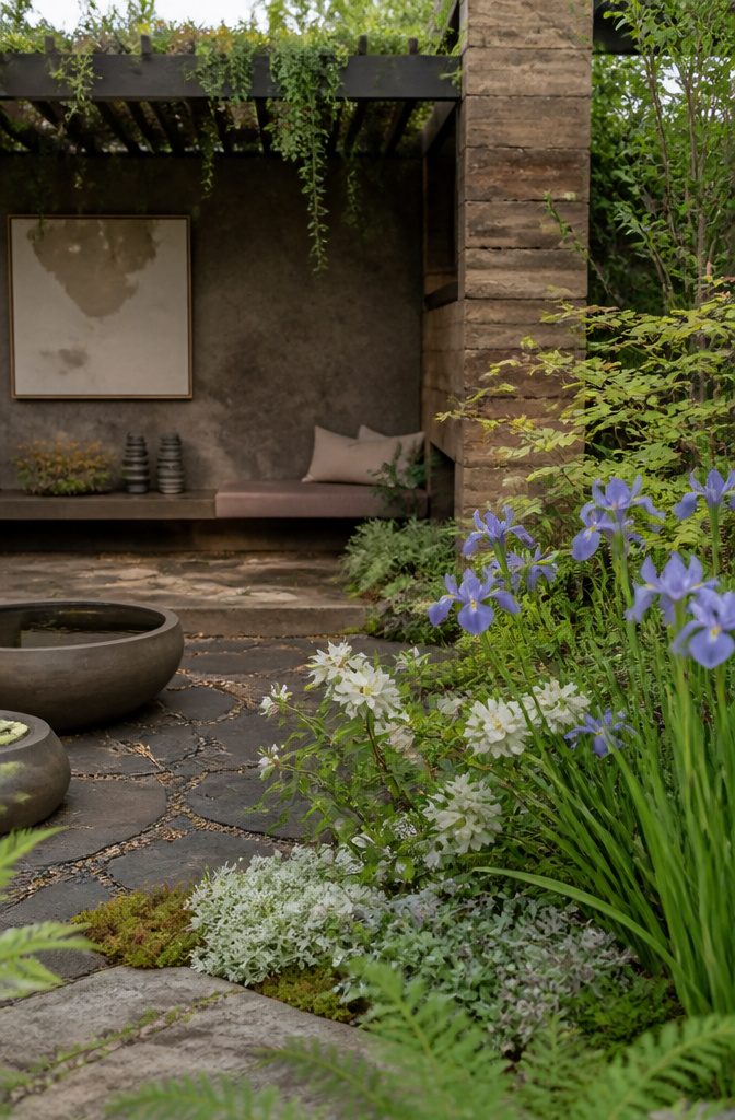 A designer explains their garden exhibit surrounded by vibrant plants.